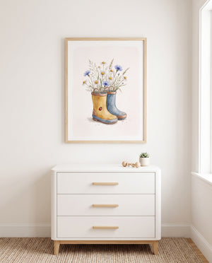 Gerahmtes Wiesenblumen-Poster mit gelbem und blauem Stiefel über einer weißen Kommode an heller Wand