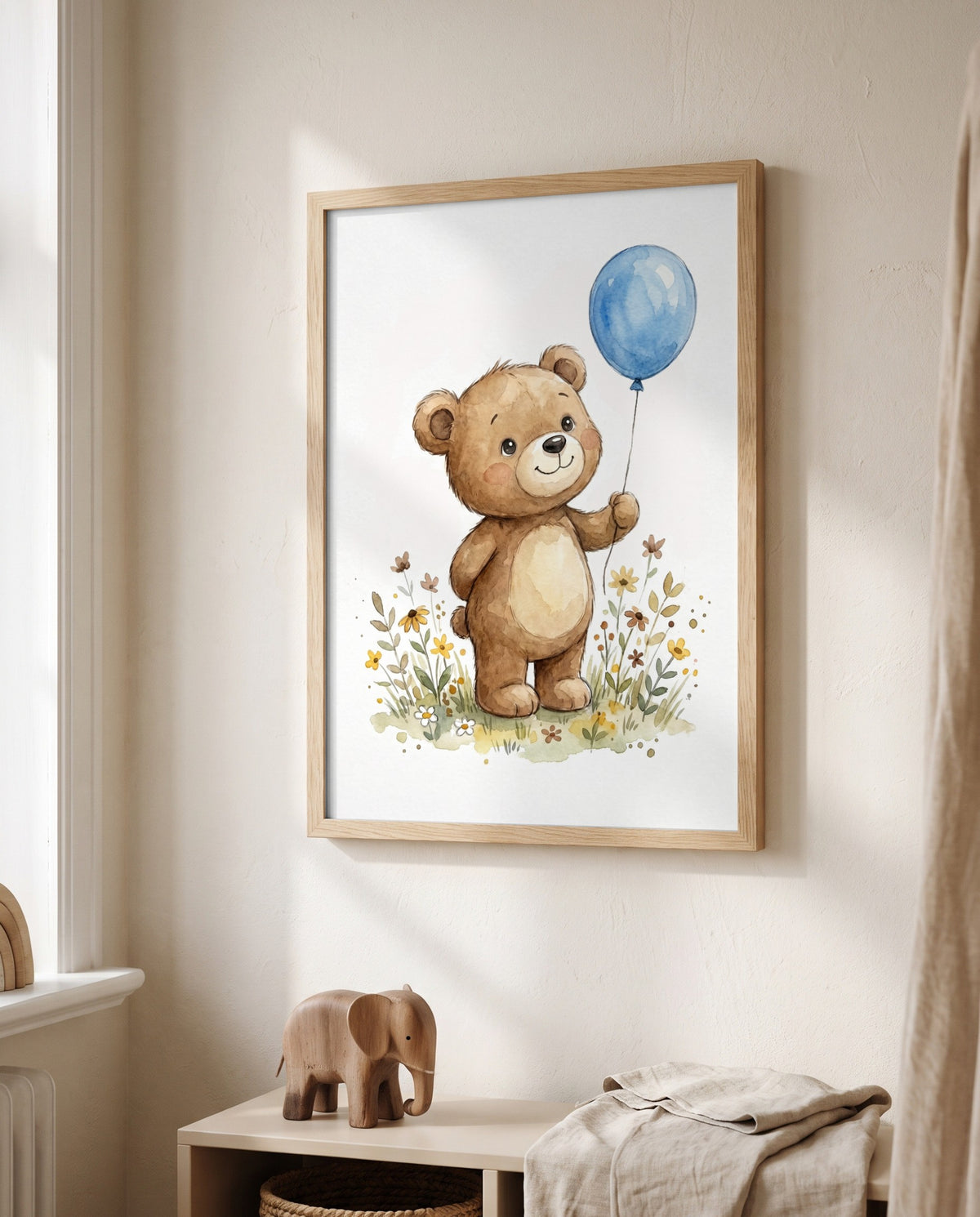 Bär mit blauem Luftballon und Blumen im hellen Holzrahmen neben einem Fenster, darunter ein niedriges Regal mit Holzelefant und gefalteten Textilien.