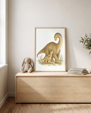 Gerahmtes Poster mit zwei Langhals-Dinosauriern auf einer niedrigen Holzkommode. Daneben sitzen ein Plüschhase und ein Bücherstapel; links ist ein Fenster, rechts sind grüne Zweige sichtbar.