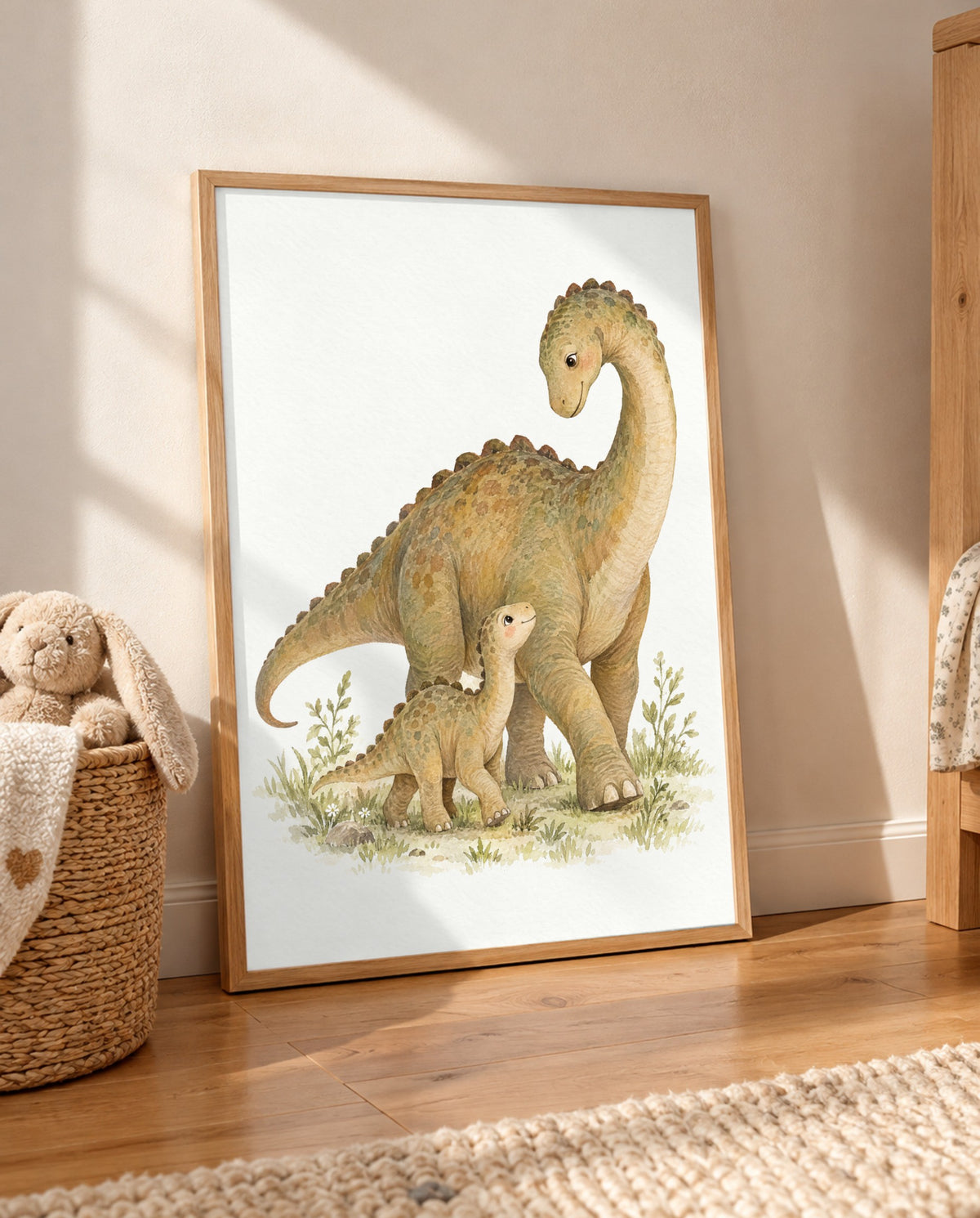 Dino-Duo-Poster im hellen Holzrahmen, auf dem Holzboden an die Wand gelehnt. Links steht ein geflochtener Korb mit Plüschhase und Decke, rechts ist ein Holzmöbel mit gemustertem Stoff sichtbar; im Vordergrund liegt ein heller Teppich.