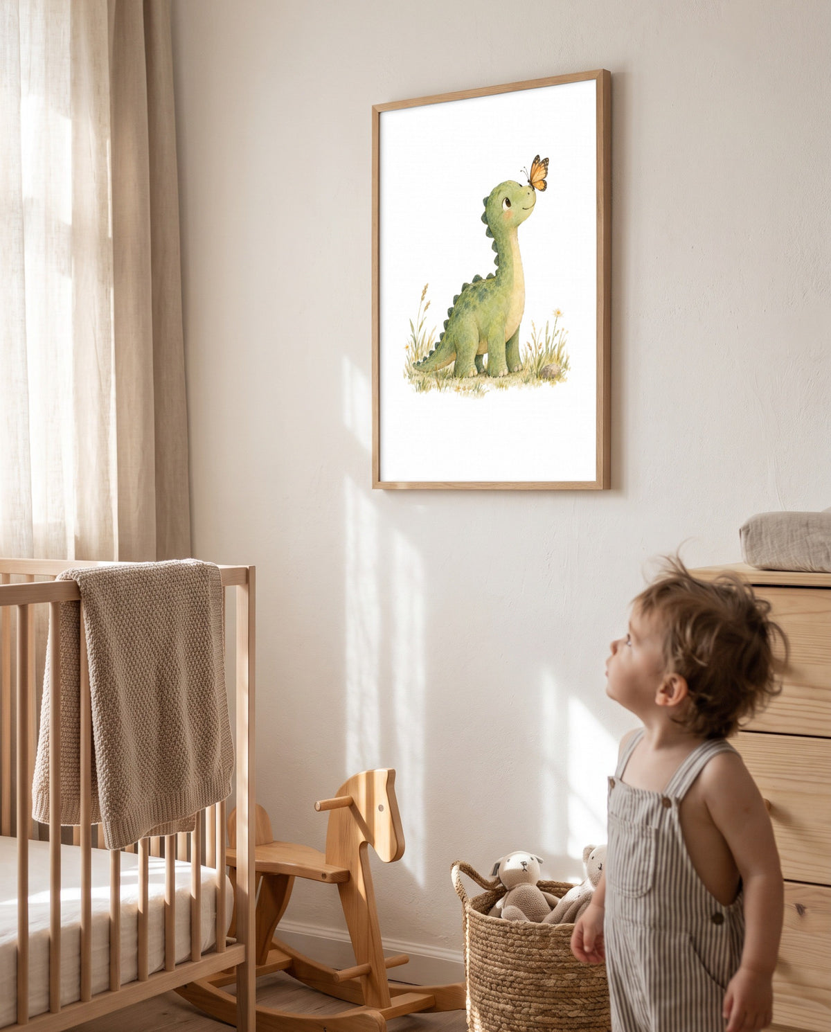 Ein Kleinkind blickt zu einem Dino-Poster mit Schmetterling im Holzrahmen hinauf; daneben stehen ein Babybett, ein hölzernes Schaukelpferd, ein Korb mit Stofftieren und eine Kommode.