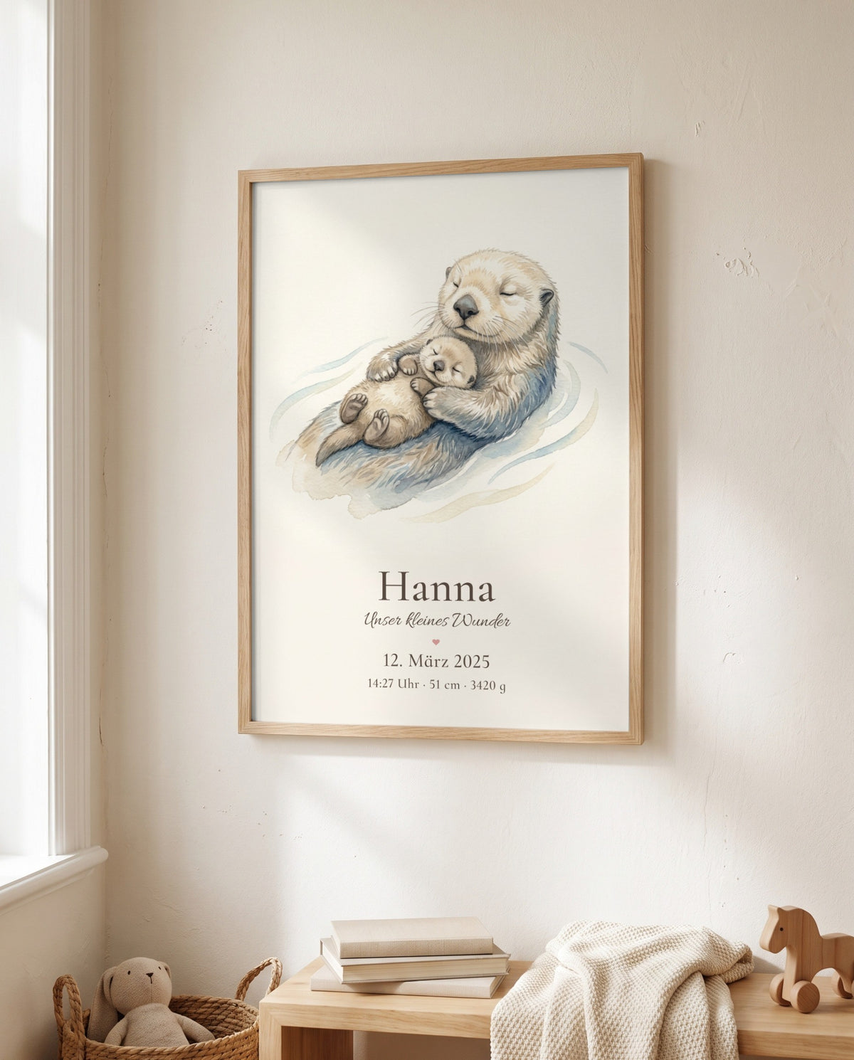 Gerahmtes Otterposter an einer hellen Wand neben einem Fenster, darunter Bücher, eine Strickdecke, ein Holzpferd und ein Stofftier im Korb.