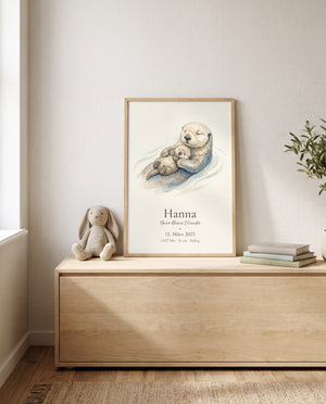 Gerahmtes Poster mit großem Otter und Jungtier auf einer niedrigen Holzkommode, daneben ein Stoffhase und ein Bücherstapel; seitlich sind Fenster und Pflanzenzweige sichtbar.