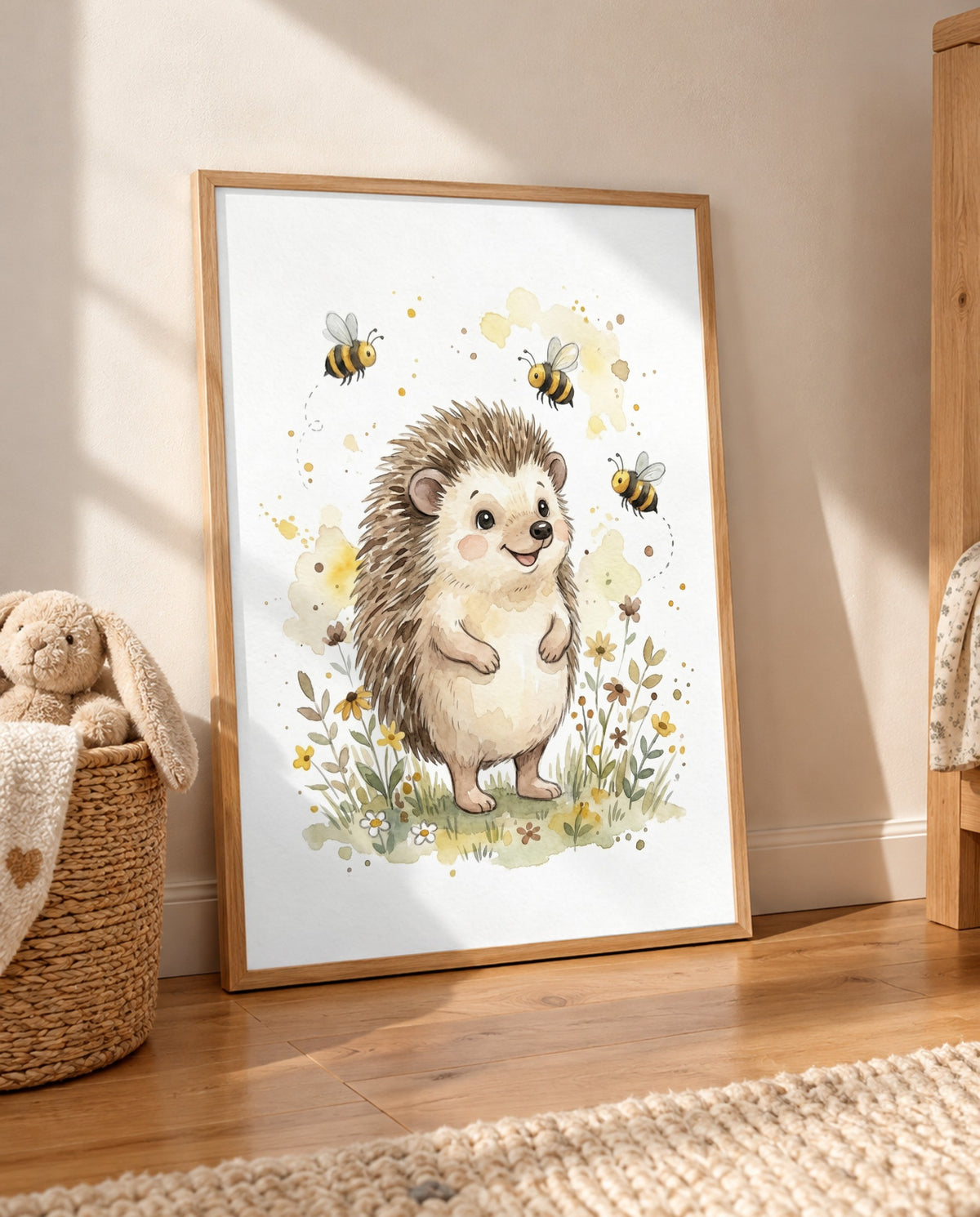 Großes Igel-und-Bienen-Poster im hellen Holzrahmen lehnt auf einem Holzboden an der Wand, neben einem Korb mit Stoffhasen und Decke; im Vordergrund liegt ein heller Teppich.