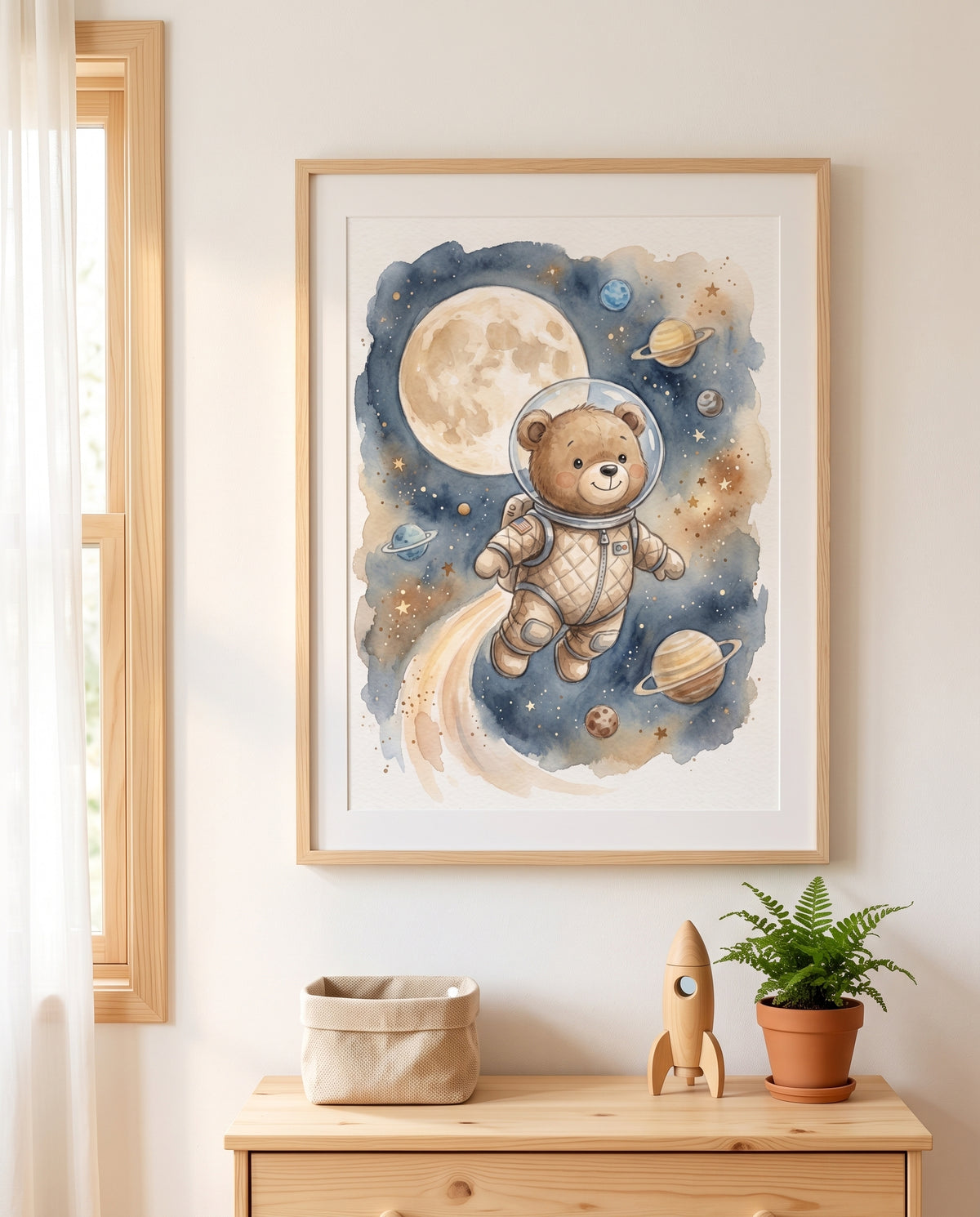 Gerahmtes Aquarellposter mit einem Bären im Astronautenanzug zwischen Mond und Planeten über einer Holzkommode. Darauf stehen ein geflochtener Korb, eine Holzrakete und ein Farn im Terrakottatopf; links ein Fenster mit hellem Vorhang.