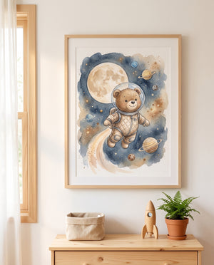 Gerahmtes Aquarellposter mit einem Bären im Astronautenanzug zwischen Mond und Planeten über einer Holzkommode. Darauf stehen ein geflochtener Korb, eine Holzrakete und ein Farn im Terrakottatopf; links ein Fenster mit hellem Vorhang.
