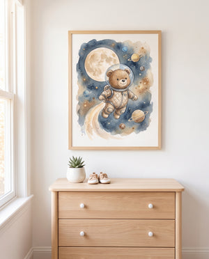 Weltraumposter mit Bär, großem Mond und Ringplaneten im hellen Holzrahmen über einer Holzkommode mit weißen Knöpfen. Auf der Kommode stehen eine Pflanze im weißen Topf und kleine Schuhe; links fällt Licht durch ein Fenster.