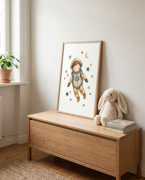 Astronautenposter mit Sternen und Mondsichel im hellen Holzrahmen, angelehnt auf einer Holztruhe. Daneben liegen Bücher und sitzt ein großer Stoffhase; auf der Fensterbank steht eine Topfpflanze.