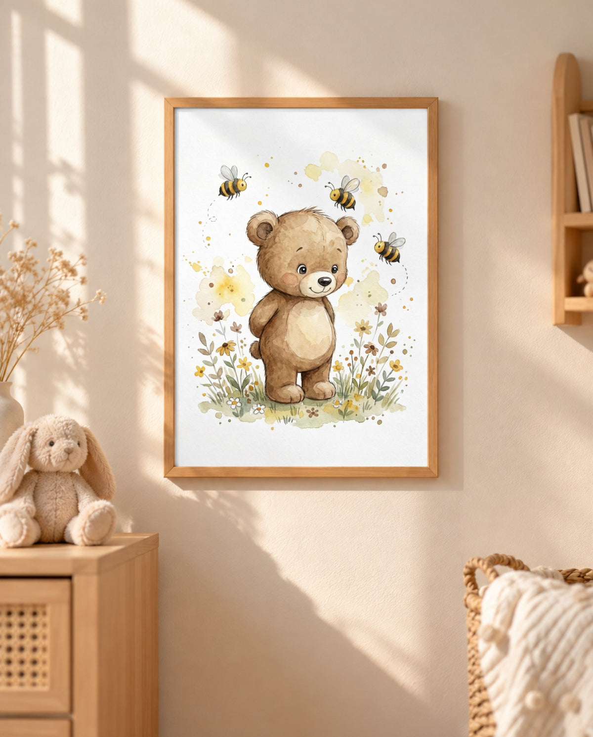 Gerahmtes Bärenposter mit drei Bienen und Wiesenblumen an einer sonnigen Wand, daneben eine Holzkommode mit Stoffhasen und Zweigen sowie ein Korb mit Decke.