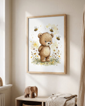 Poster mit Bär, drei Bienen und Blumen im hellen Holzrahmen neben einem Fenster, darunter ein niedriges Regal mit Holzelefant, Korb und hellem Stoff.