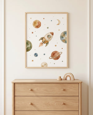 Gerahmtes Weltraumposter mit Rakete, Planeten, Mondsichel und Sternen über einer Holzkommode mit runden Knöpfen, kleinem Holzobjekt und Regenbogendekoration.