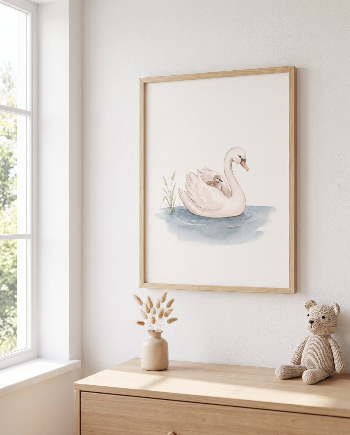 Gerahmtes Schwanmotiv mit Küken über einer Holzkommode neben einem Fenster. Auf der Kommode stehen eine kleine Vase mit Trockenblumen und ein gestrickter Teddybär.